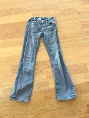 Grå bootcut jeans med fickdetaljer - Snygga grå bootcut jeans. Jeansen har låg midja och utsvängda ben, som ni kan se på fjärde bilden finns det ett litet hål på högra sidan av högra benet💕