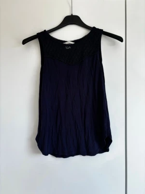 Mörkblå ärmlös linnetopp - Snygg mörkblå linnetopp med rund halsringning och dekorativt mönstrad överdel. Toppen är ärmlös och har en avslappnad passform, perfekt för varma dagar. Materialet känns lätt och luftigt.