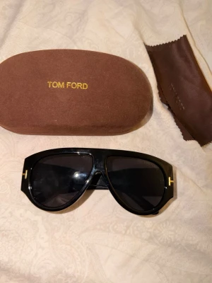 Svarta Tom Ford aviator solglasögon - Snygga svarta solglasögon från Tom Ford med klassisk pilotform och guldfärgade detaljer vid gångjärnen. Bågarna är tillverkade i plast och glasen är mörka. Kommer med originalfodral och putsduk.