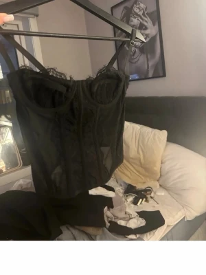 Svart spetsbody från SHEIN - Snygg svart body från SHEIN med tunna axelband och detaljer i spets. Modellen har bygelkupor och transparent meshmaterial som ger en trendig look. Perfekt för dig som vill ha något extra under kläderna. Spetsen ger en feminin touch och passformen är figurnära.