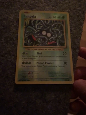 Tangela Pokémonkort - Tangela Pokémonkort från originalserien. Kortet har en grön ram och visar Tangela med sina blå slingrande rankor och vita ögon. Text och attacker på engelska. Perfekt för samlare eller Pokémonfans.
