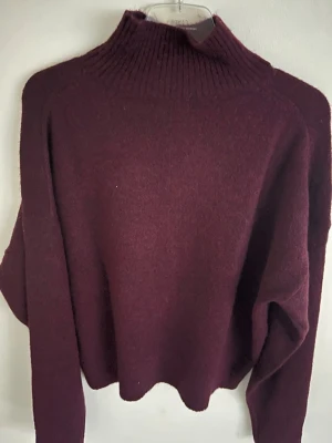 Vinröd polotröja - Mysig vinröd stickad polotröja med hög ribbad krage och långa ärmar. Tröjan har en avslappnad passform och är tillverkad i en mjuk ullblandning som håller dig varm under kyliga dagar. Storlek S men skulle nog passa xs också