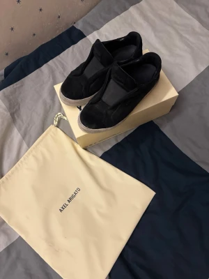 Svarta slip-on sneakers Axel Arigato - Stilrena svarta slip-on sneakers från Axel Arigato i mocka med vit sula. Klassisk låg modell utan snörning, perfekt för en clean och modern look. Kommer med originalpåse och låda.