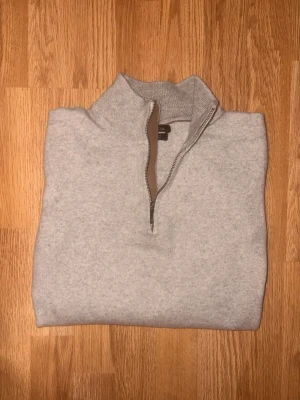 Kaschmir halvzip Massimo Dutti - Ljusgrå kaschmir tröja med halvzip och hög krage. Tröjan är från Massimo Dutti och har långa ärmar och en stilren design som passar perfekt till lager-på-lager. Materialet ser mjukt och bekvämt ut, och dragkedjan har en snygg kontrastkant.