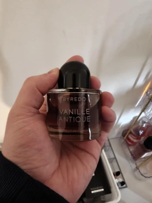 Byredo Vanille Antique parfym första utgåva  - Byredo Vanille Antique är en lyxig parfym i en rund glasflaska med mörkbrun ton och svart rund kork. Flaskan har en stilren design med tydlig vit text på framsidan. Doften är känd för sina varma vaniljtoner och exklusiva känsla.