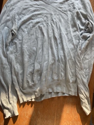 Blå stickad tröja Tiger of Sweden - Ljusgrå stickad tröja från Tiger of Sweden med v-ringad hals och långa ärmar. Tröjan har ribbade muddar vid ärmslut och nederkant. Perfekt för dig som gillar stilrena och klassiska plagg.