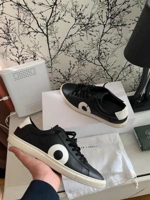Svarta sneakers från Oliver Cabell - Stilrena svarta sneakers från Oliver Cabell med vit sula och stor vit cirkeldetalj på sidan. Skorna har svarta skosnören och vit hälflik. Tillverkade i slätt läder för en clean look som passar till det mesta.