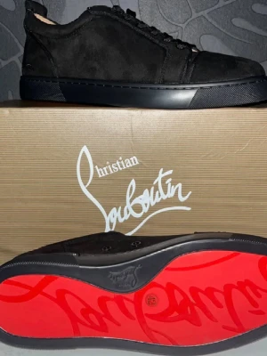 Svarta sneakers från Christian Louboutin - Snygga svarta sneakers från Christian Louboutin i mocka med den ikoniska röda sulan och diskret logga på sidan. Lågt skaft och klassisk siluett som passar till det mesta. Skorna har svarta snören och en stilren design.