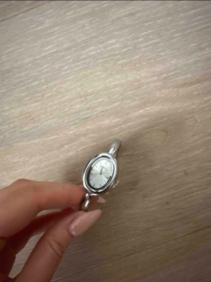 silverfärgad klocka - Armbandsklocka med oval urtavla i vitt och smalt silverfärgat armband. 