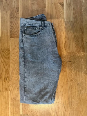 Grå raka jeans - Säljer ett par grå jeans med rak passform och klassisk femficksdesign. Jeansen har en snygg tvättad look och är tillverkade i denim. Perfekta för dig som gillar en avslappnad och tidlös stil.