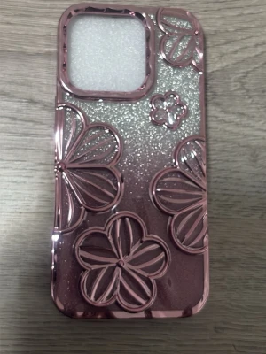  mobilskal iPhone 16 PRO  - Snyggt mobilskal i metallic rosa med glittrig bakgrund och upphöjda blommönster. Skalets yta är blank och ger ett trendigt intryck, perfekt för dig som vill sticka ut. Passar till mobil med stor kameraöppning. Materialet är plast. 