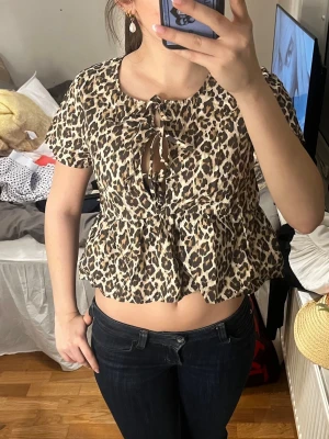 Leopardmönstrad blus med volang - Säljer en leopardmönstrad blus med korta ärmar och volang nedtill. Blusen har knytning framtill och en lätt rynkad midja som ger en söt och trendig look. Perfekt för dig som vill sticka ut med ett djurmönster. Materialet känns lätt och luftigt.