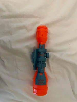 Nerf kikarsikte plast orange/blå - Säljer ett kikarsikte till Nerf i plast, färgerna är orange och blå. Siktet har detaljerad design med ratt på sidan och ventilationshål. Perfekt tillbehör för att uppgradera din Nerf-blaster och få bättre precision.