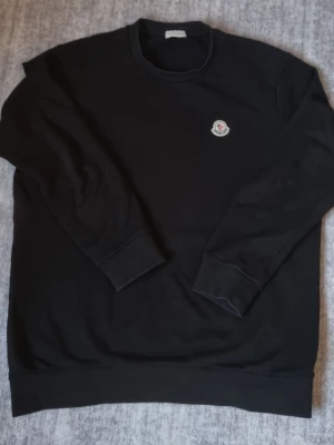 Svart stickad tröja från Moncler - Svart långärmad tröja från Moncler med rund halsringning och Moncler-logga broderad på bröstet. Tröjan har långa ärmar och ribbade muddar vid ärmslut och nederkant. Perfekt för en stilren och enkel look. NFC funkar. Äkta tröja som jag fick som present för c.a 4,000kr.
