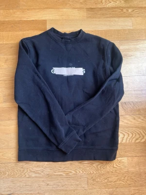 Svart sweatshirt från H&M - En svart sweatshirt från H&M med tryck framtill. Tröjan har rund halsringning, långa ärmar och ribbade muddar vid ärmslut och nederkant. Perfekt för en avslappnad och stilren look.