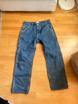 Blå loose fit jeans från 157 - Säljer ett par klassiska blå jeans från 157 med loose fit och raka ben. Jeansen har flera fickor, inklusive en stor bakficka och verktygsficka på sidan. Perfekta för en avslappnad och trendig look. Tillverkade i bomull.