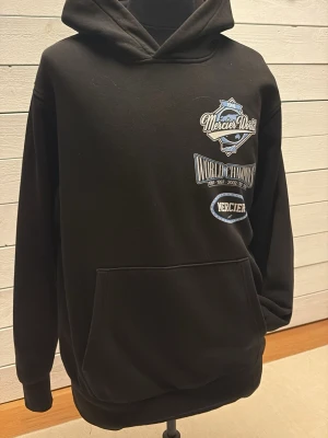 Svart hoodie från Mercier - Svart hoodie från Mercier med tryckt  i vitt och blått både fram och bak. Klassisk känguruficka och puffig huva. Hoodien har en relaxed passform och är tillverkad i mjuk bomullsmix, perfekt för en chill och stilren look.