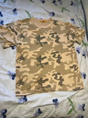 Beige camo t-shirt - Säljer en beige och grön camo t-shirt med klassiskt rund halsringning och korta ärmar. Perfekt för dig som gillar streetwear och vill sticka ut lite extra. Skön passform och mjukt material.