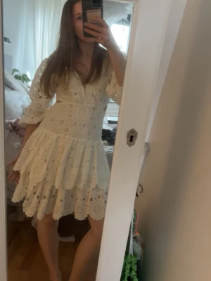 Maje klänning - Söt vit kortklänning med broderad spets, v-ringning och volangkjol. Klänningen har trekvartsärm och öppen ryggdetalj. Perfekt för sommarens alla tillfällen och ger en romantisk vibe. Det är en äkta maje klänning i storlek 36.