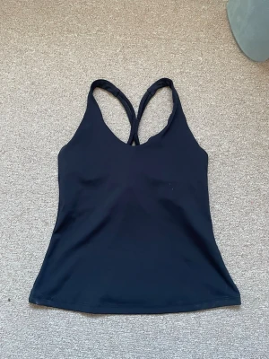 Sportig svart linnetopp med korsade band - Snygg svart linnetopp från Casall med smala korsade axelband i ryggen. Tillverkad i ett stretchigt syntetmaterial som passar perfekt för träning. 