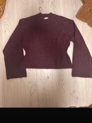 Mörkröd stickad tröja från Gina M (+14) - Mysig mörkröd stickad tröja med lång ärm och rak passform. Tröjan har en enkel design utan synliga detaljer och är perfekt för lager-på-lager. Materialet ser ut att vara mjukt och passar bra till kyligare dagar.