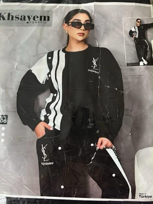 Svartvitt loungewear-set från Khsayem - Snyggt svartvitt loungewear-set från Khsayem med vågiga och raka ränder i vitt och svart. Setet består av en långärmad tröja och matchande byxor med tryckknappar längs sidorna. Båda plaggen har tryckt logga och text. Perfekt för chill dagar hemma.