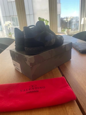 Valentino Rockrunners  - Snygga sneakers från Valentino Garavani i svart och mörkblå camo-design. Skorna har lågt skaft, klassisk snörning och detaljer i mocka och läder. Kommer med originalkartong och röd dustbag med logga. Pris kan diskuteras!