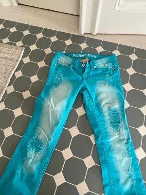 Turkosa slitna jeans från Antique Rivet - Säljer ett par turkosa jeans från Antique Rivet med slitningar på benen. Aldrig använda men köpta från Sellpy prislapp finns kvar