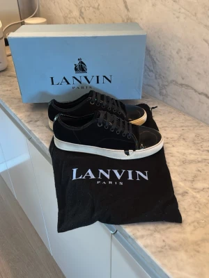 Svarta Lanvins - Snygga svarta sneakers från Lanvin med vita sulor och glansiga lackdetaljer på tån. Skorna har en lite trasig sula men den går att laga för någon hundring. Utöver sulan är skorna i 10/10 skick. Skorna är storlek 40 men stora i storlek så de borde även passa 41-42. Pris går att diskutera! Ingår 1st dustbag!