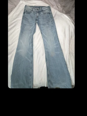 Ljusblå bootcut jeans - Säljer ett par ljusblå bootcut jeans med klassisk femficksmodell och hög midja. Jeansen har en snygg tvättad look och vida ben som ger en retrovibe. Perfekta för dig som gillar en avslappnad men trendig stil.