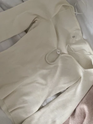 Vit ribbad långärmad topp H&M - Trendig vit ribbad topp från H&M med lång ärm och en snygg cut-out detalj framtill vid halsen. Toppen har en figurnära passform och är tillverkad i mjukt stretchigt material som känns bekvämt mot huden. Perfekt att styla med jeans eller kjol.