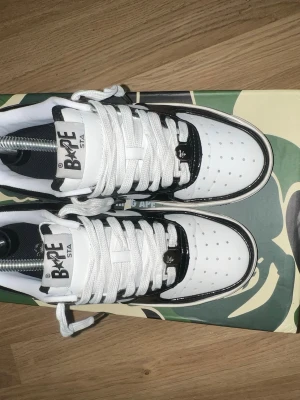 BAPE STA svartvita sneakers - Säljer ett par BAPE STA sneakers i svart och vitt med klassisk stjärndesign på sidan. Skorna har vita snören, perforerad tåbox och tydliga BAPE-detaljer på plösen och snörningen. Kommer med originalkartong i camomönster och dustbag.