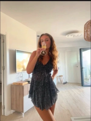 Mörkblå volangklänning med v-ringning - Söt mörkblå mönstrad topp och kjol med inbyggda shorts, med volanger och v-ringad hals. Setet har smala axelband och ett lätt, luftigt tyg som ger en avslappnad känsla. Perfekt för varma dagar och somriga tillfällen.