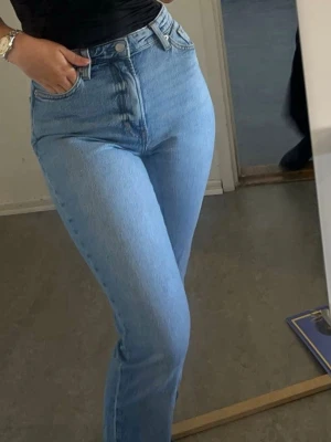 Ljusblå high waist raka jeans - Säljer ett par ljusblå jeans med hög midja och raka ben. Jeansen har klassisk femficksdesign och råa, avklippta benslut för en trendig look. Perfekta till en avslappnad stil och passar till det mesta. Materialet är denim i bomull.