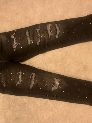Svarta distressed jeans Supply & Demand - Säljer ett par svarta jeans från Supply & Demand med kraftiga slitningar och trasiga detaljer på benen. Jeansen har även vita färgstänk för en extra edgy look. Tillverkade i bomullsmix och har skinny fit-modell.