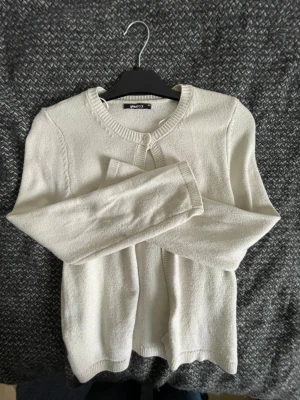 Vit kofta från Gina Tricot - Klassisk vit kofta från Gina Tricot med rund halsringning och ribbade muddar. Koftan har en enkel knappstängning framtill och är tillverkad i ett mjukt, tunt stickat material som passar perfekt till lager på lager.