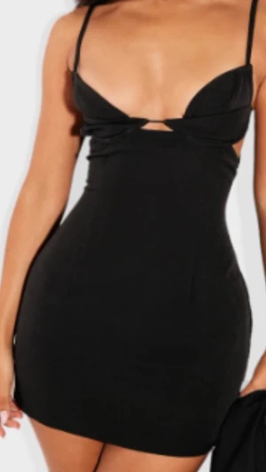 Svart kort klänning med cut out - Säljer en svart, tight kort klänning med tunna axelband och en snygg cut out-detalj framtill. Klänningen har en figurnära passform och är perfekt för dig som vill ha en stilren men ändå edgy look. Materialet känns mjukt och stretchigt.