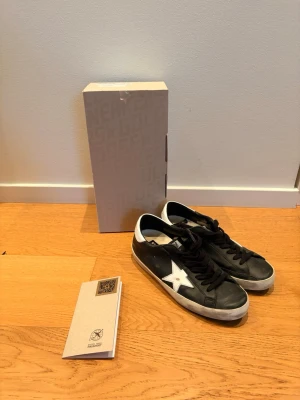 Golden Goose svarta  - Svarta sneakers från Golden Goose med vit stjärna på sidan och vit häl. Klassisk låg modell med svarta skosnören och slitstark gummisula. Skorna har en cool vintage-look och är tillverkade i läder. 100% äkta golden goose då de är köpta i butik. 