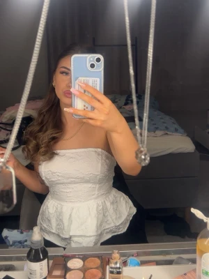 Vit axelbandslös peplum topp med rosett - Säljer en söt vit axelbandslös topp med peplum och stor rosett i ryggen. Toppen har en strukturerad yta med diskret mönster och är perfekt för dig som vill ha en feminin och trendig look. Passar till både jeans och kjol.