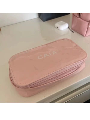 Ljusrosa necessär från CAIA - Säljer en ljusrosa necessär från CAIA med dragkedja runt om. Väskan har en rektangulär form och är tillverkad i ett glansigt material, perfekt för smink eller småprylar. Enkel och stilren design med CAIA-logga på ovansidan.