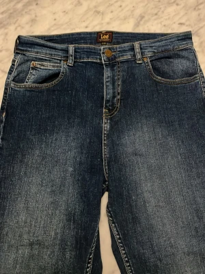 Blå raka jeans från Lee - Klassiska blå jeans från Lee med rak passform och fem fickor. Jeansen har en snygg tvättad look och detaljer i kopparfärgad metall. Tillverkade i slitstark denim med Lee-lapp bak i midjan. Perfekta till vardagsstilen.