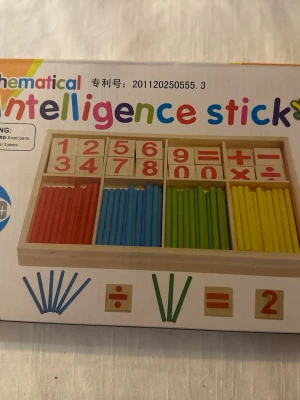 Matematiskt träspel med färgpinnar - Säljer ett pedagogiskt matematikspel i trä med färgglada pinnar i rött, blått, grönt och gult samt träbrickor med siffror och räknesymboler. Perfekt för att öva på enkel matematik och räkning på ett roligt sätt. Allt ligger i en praktisk trälåda.