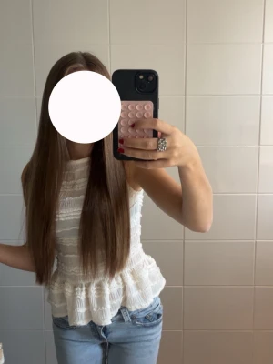 Vit volang topp med struktur - Säljer en söt vit topp med volangkant och strukturerat tyg. Toppen är ärmlös och har en lätt peplumformad nederdel som ger en feminin siluett. Perfekt att matcha med jeans eller kjol för en fräsch look.