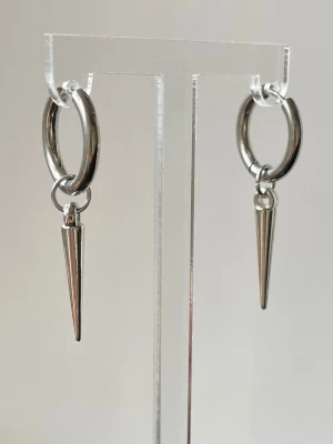 Silvriga hoops med spetsiga hängen - Säljer ett par coola örhängen i rostfritt stål,silvriga hoops, allergi vänliga med avlånga, spetsiga hängen. Örhängena har en minimalistisk och edgy design som sticker ut. Perfekta för dig som gillar en stilren men ändå tuff look. 