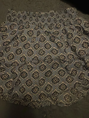 Mönstrad blå kjol med resårmidja - Säljer en flowy kjol med blått och vitt orientaliskt mönster. Kjolen har bred resår i midjan för skön passform och är gjord i ett lätt material som passar perfekt till varma dagar. Mönstret ger en bohemisk vibe och kjolen är enkel att styla med en enkel topp.