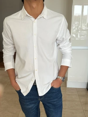 Vit klassisk skjorta i bomull - Säljer en stilren vit skjorta med klassisk krage och knappar framtill. Skjortan är långärmad och har en normal passform, perfekt till jeans eller chinos. Tillverkad i mjuk bomull för en bekväm känsla.