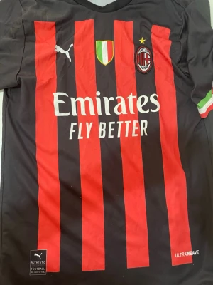 AC Milan Ibrahimović matchtröja Puma - Snygg AC Milan matchtröja från Puma med röda och svarta ränder, klubbmärke och sponsortryck på bröstet. På ryggen står Ibrahimović och nummer 11. Italienska flaggan på ärmen och bröstet. Tillverkad i lätt och funktionellt material.