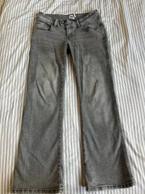 Grå bootcut jeans från 157 - Snygga grå bootcut jeans från 157 med klassisk femficksdesign och dubbla knappar i midjan. Jeansen har en lätt tvättad look och raka ben med lite utsvängd passform. Perfekta för dig som gillar en avslappnad men trendig stil.