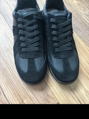 Maison Margiela svarta sneakers - Säljer ett par svarta Maison Margiela i storlek 39. Helt nya, aldrig använda. Hör av dig vid fråga eller nya bilder!! 