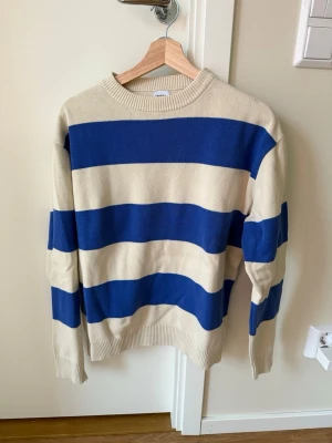 Randig stickad tröja - Stickad tröja med breda blå och creme vit ränder. Tröjan har rund halsringning, långa ärmar. Passar S/M